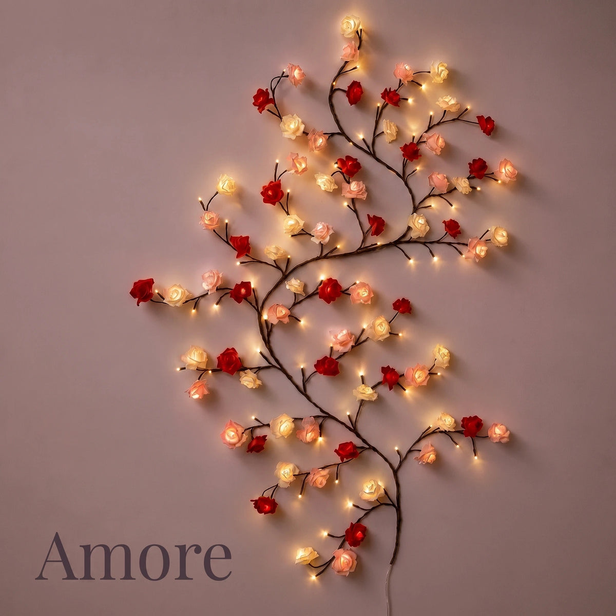 Guirnalda Amore Lights encendida con luz cálida sobre una pared en penumbra, con sus rosas rojas, crema y empolvadas