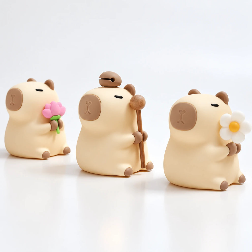 Tres Capibara Glow en fila, uno con flor de loto, otro con el mazo y otro con la margarita