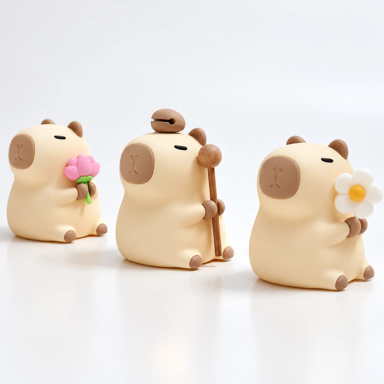 Tres Capibara Glow en fila, uno con flor de loto, otro con el mazo y otro con la margarita