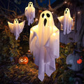 Varios fantasmas Ghost Glow colgados en un porche entre calabazas, encendidos de noche