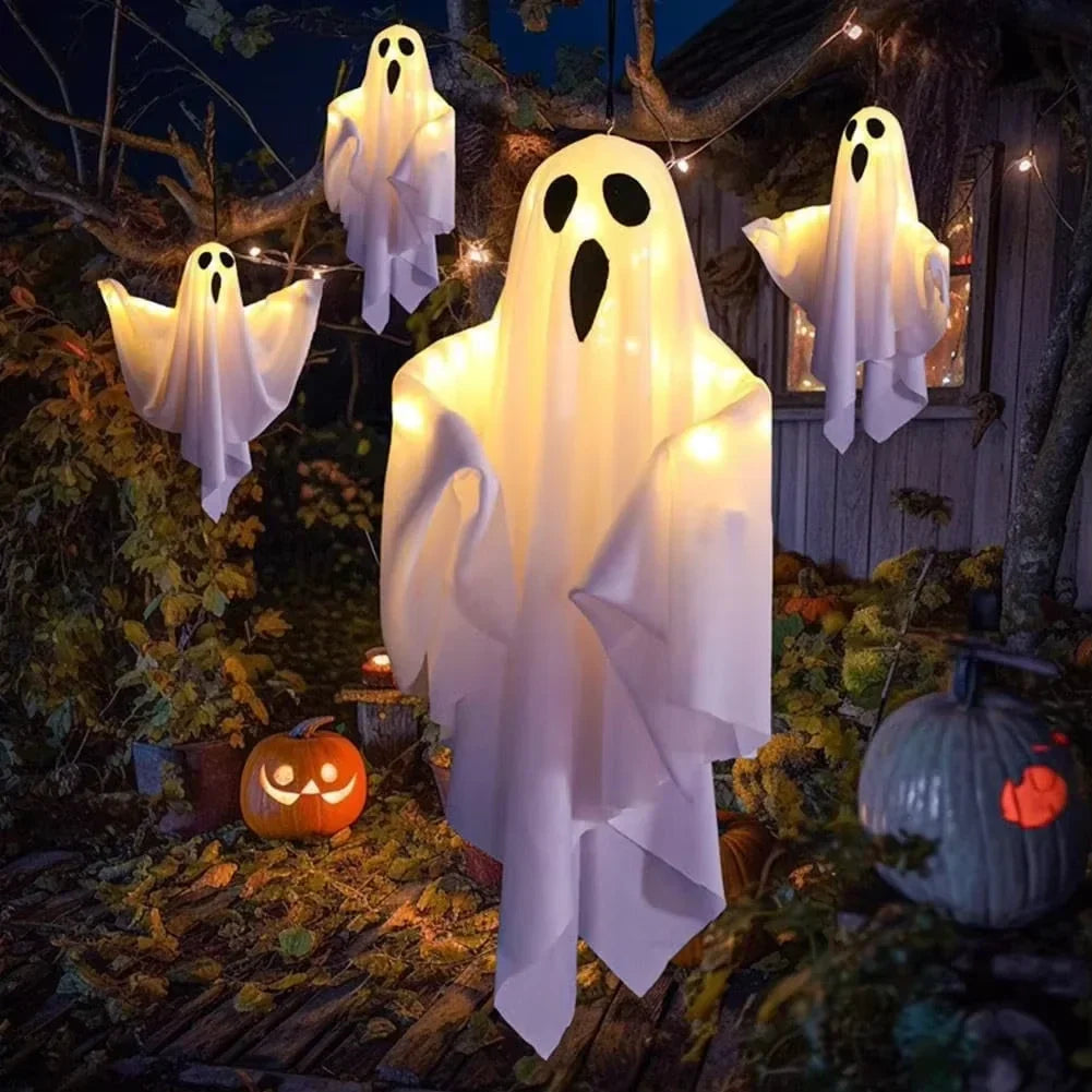 Fantasmas Ghost Glow colgados en un porche entre calabazas, encendidos de noche