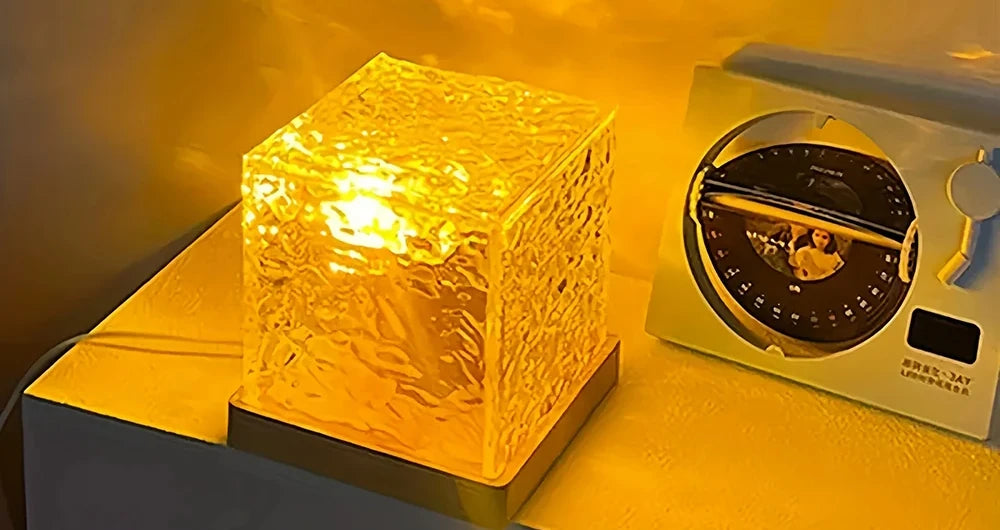 El cubo encendido en luz cálida sobre una mesa, proyectando ondas de agua en la pared